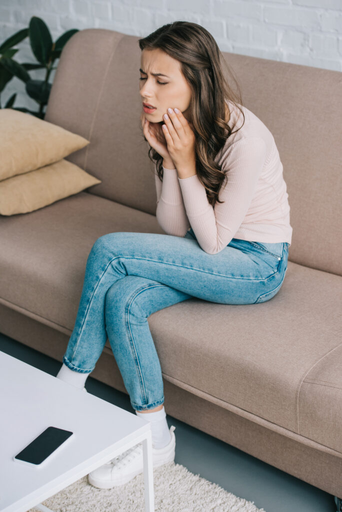 woman sitting on couch wincing in pain