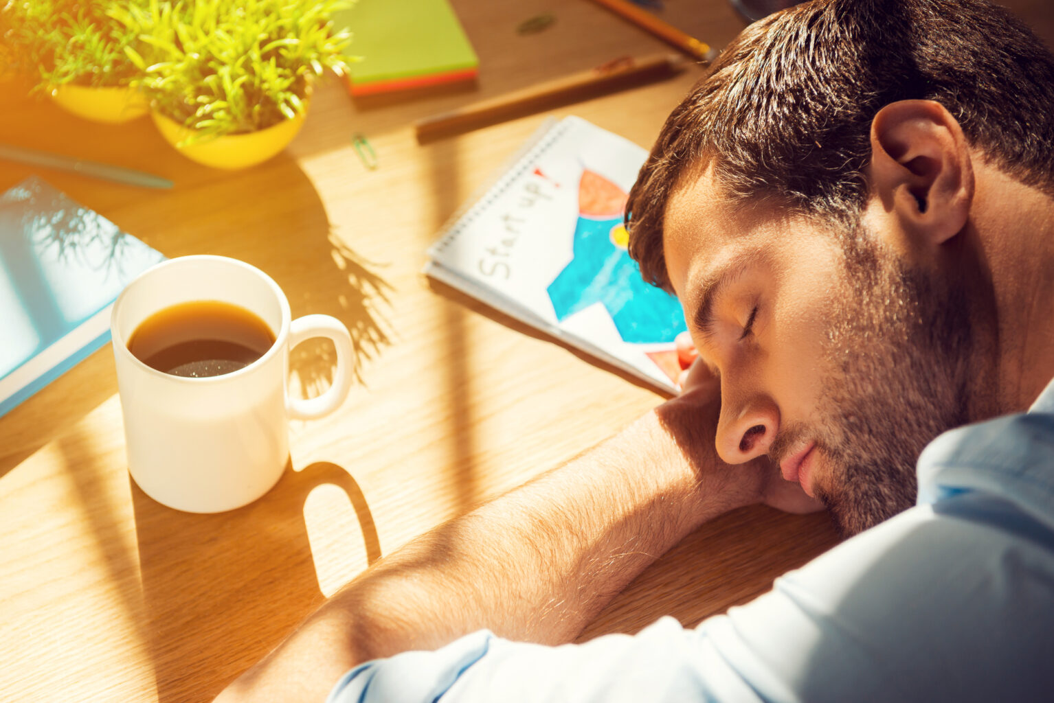 man sleeping on desk with cup of coffee