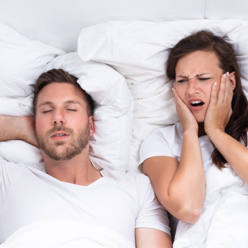 Woman Covering Her Ears While Man Snoring (a sign of sleep apnea)