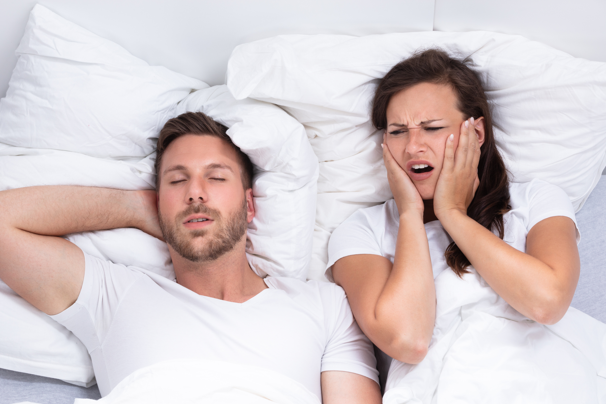 Woman Covering Her Ears While Man Snoring (a sign of sleep apnea)