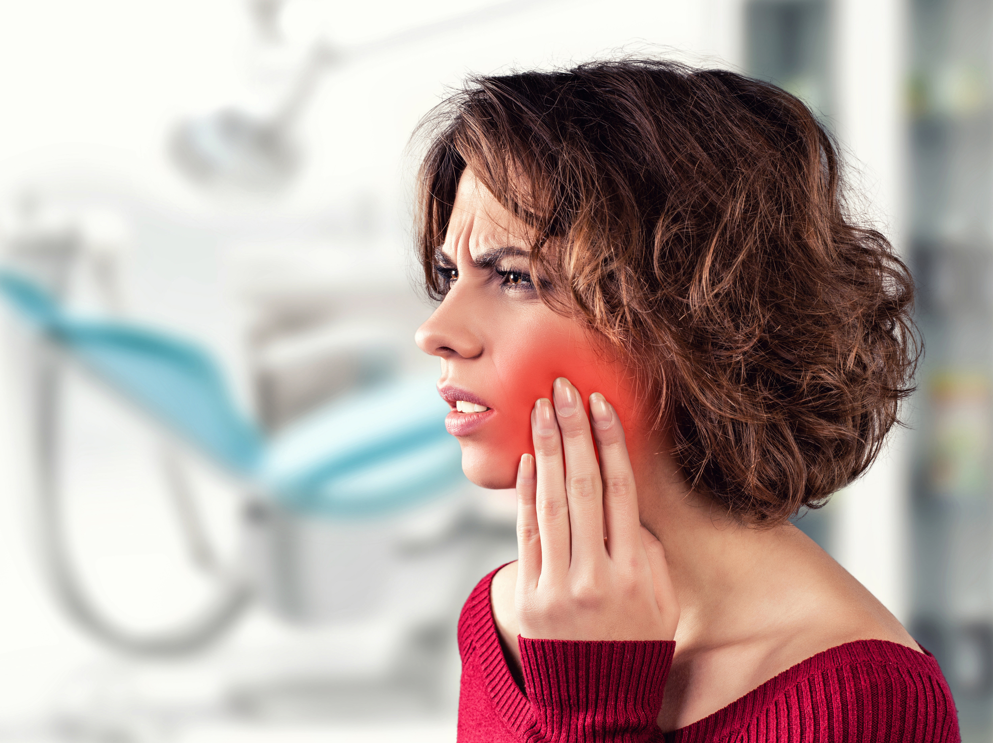 A woman clutches the side of her face, indicating orofacial pain.