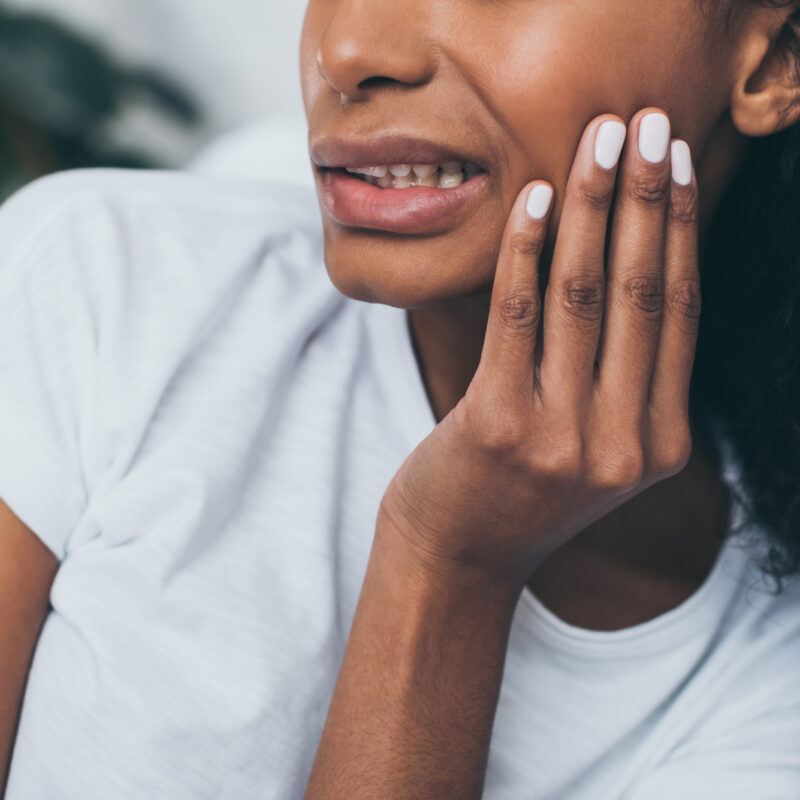 A Black woman clutches her jaw, indicating a temporomandibular disorder (TMD)
