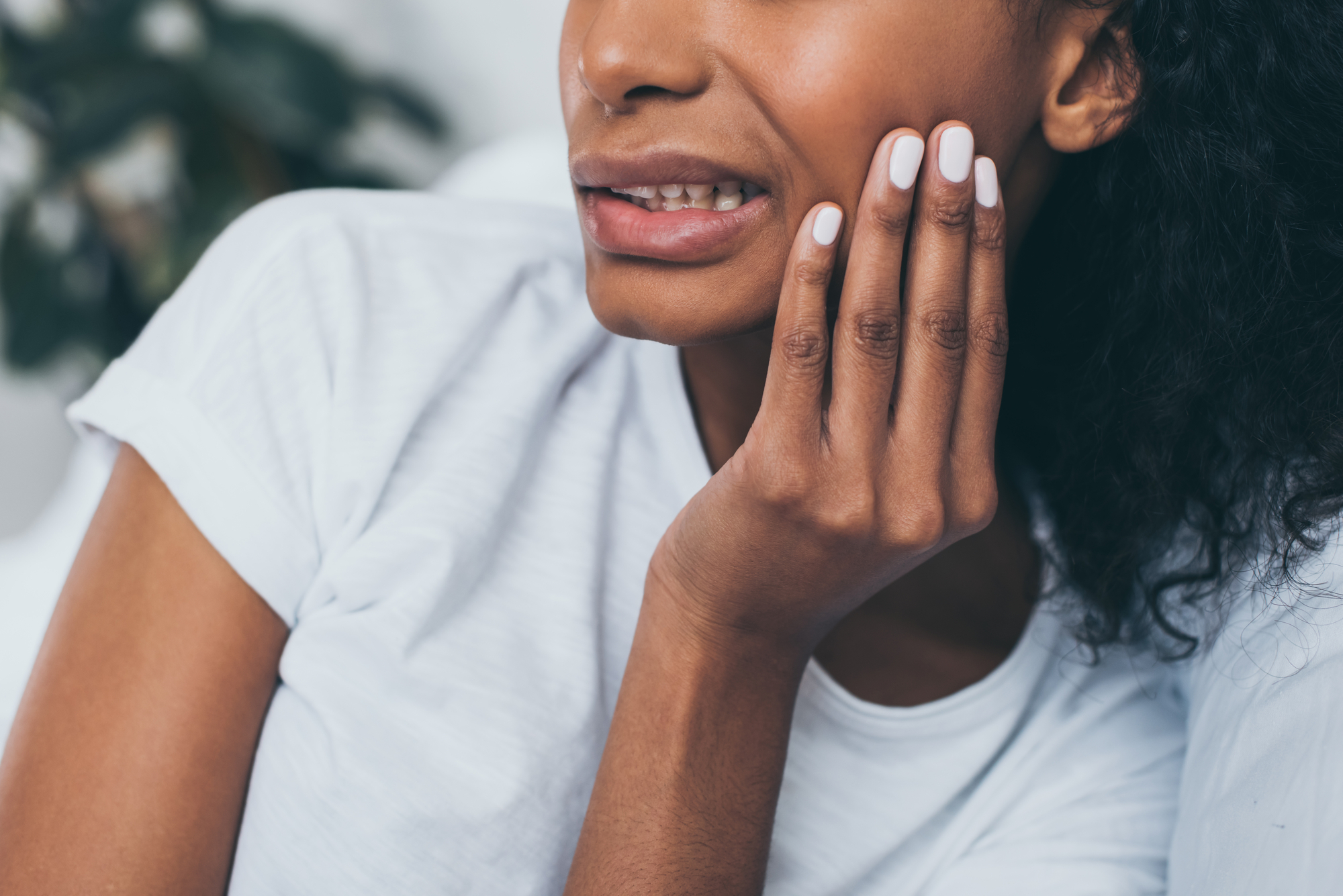 A Black woman clutches her jaw, indicating a temporomandibular disorder (TMD)