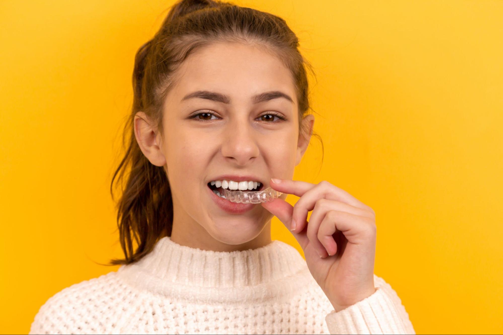 A young woman places a clear aligner in her mouth after getting Invisalign in Sacramento, CA