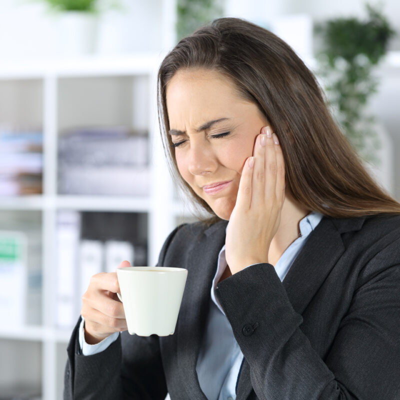 woman with tmj disorder wincing while drinking coffee