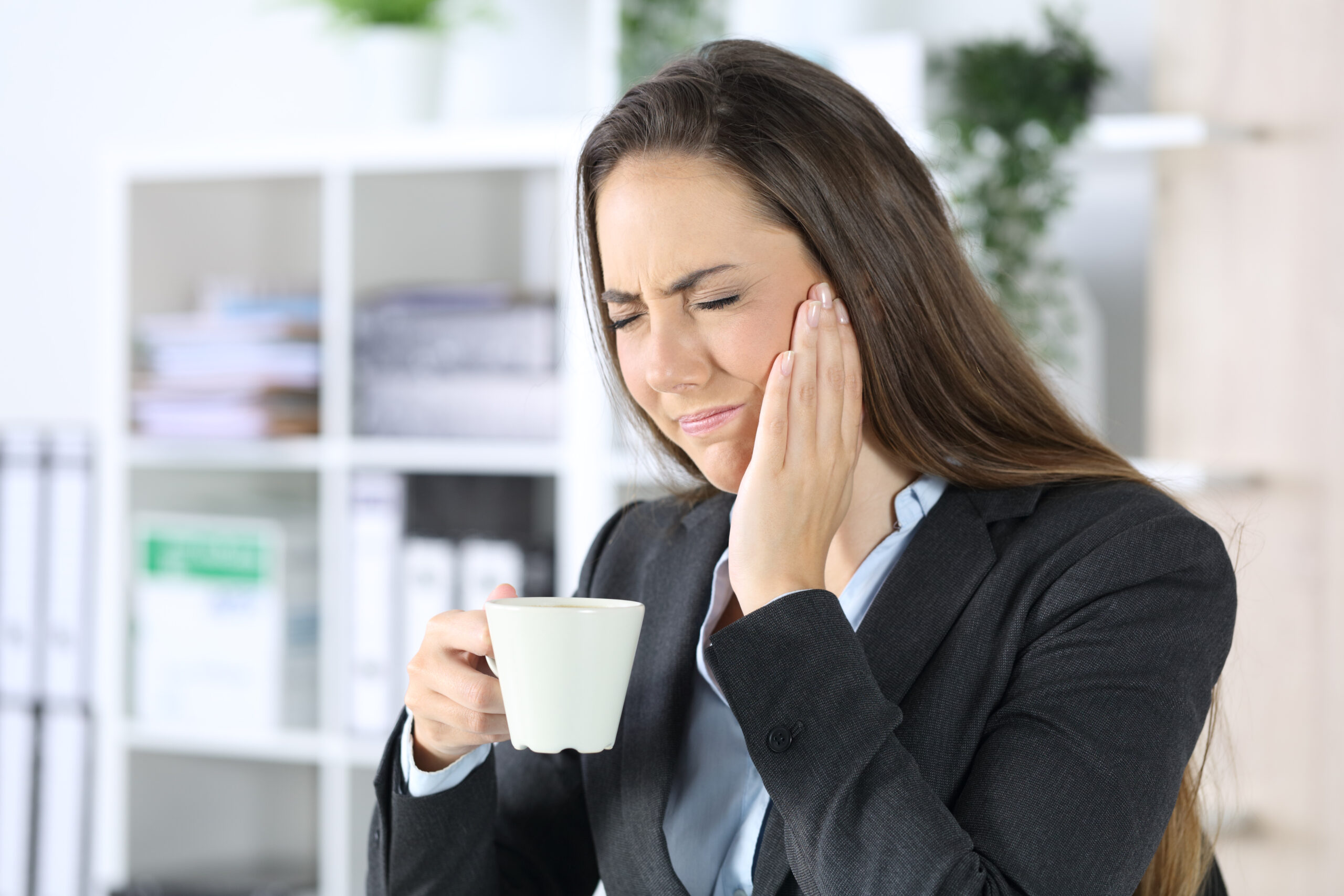 woman with tmj disorder wincing while drinking coffee