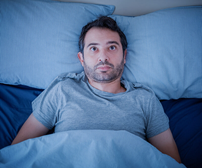 awake man in bed needs insomnia treatment to sleep