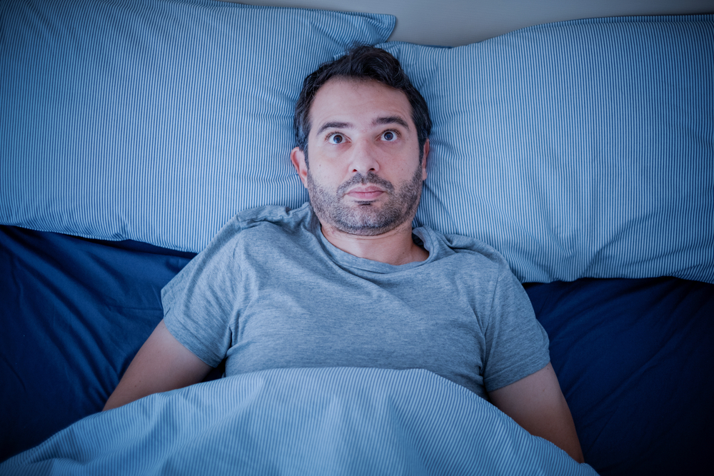 awake man in bed needs insomnia treatment to sleep