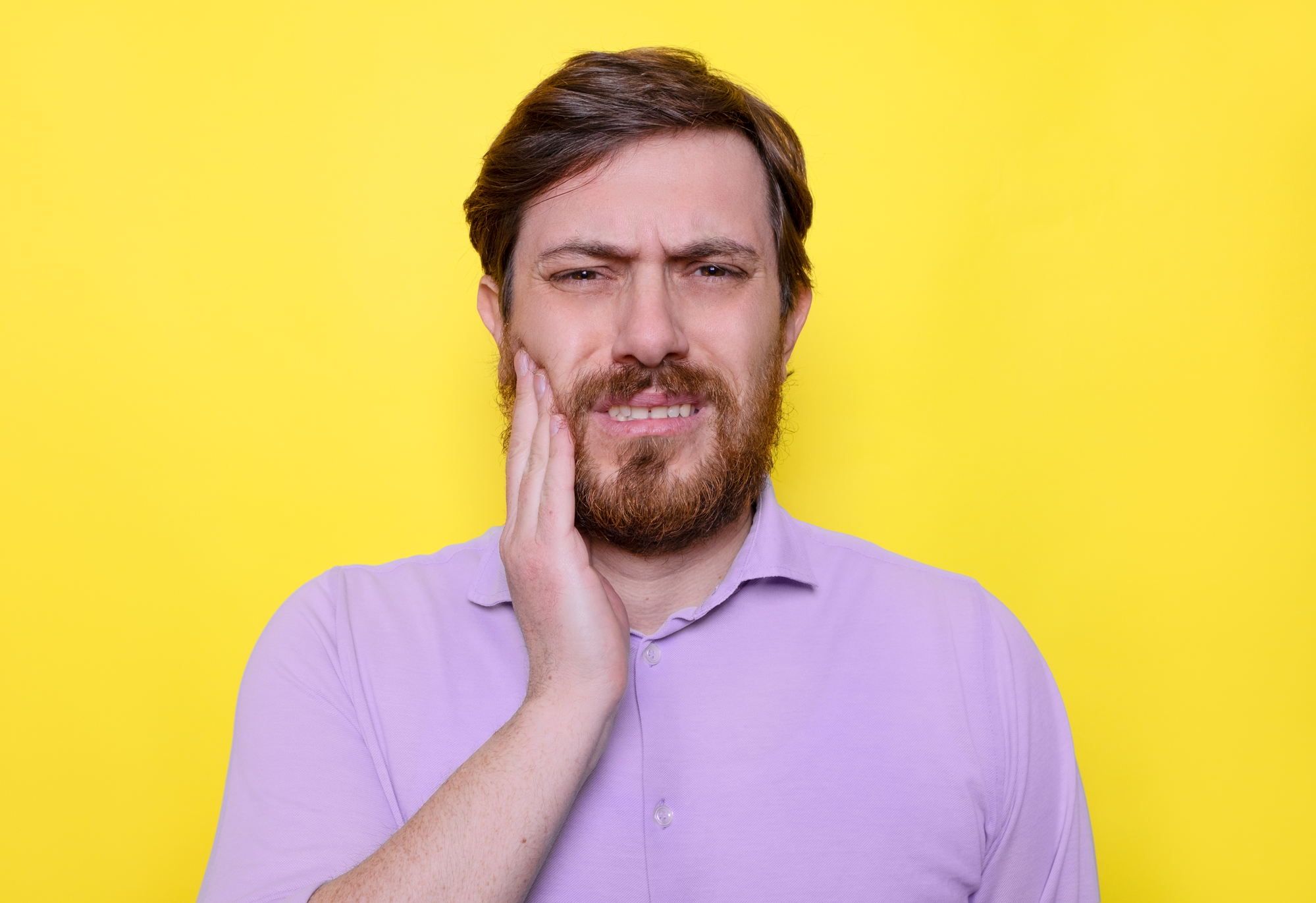 man in pink shirt with hand on his jaw on yellow background