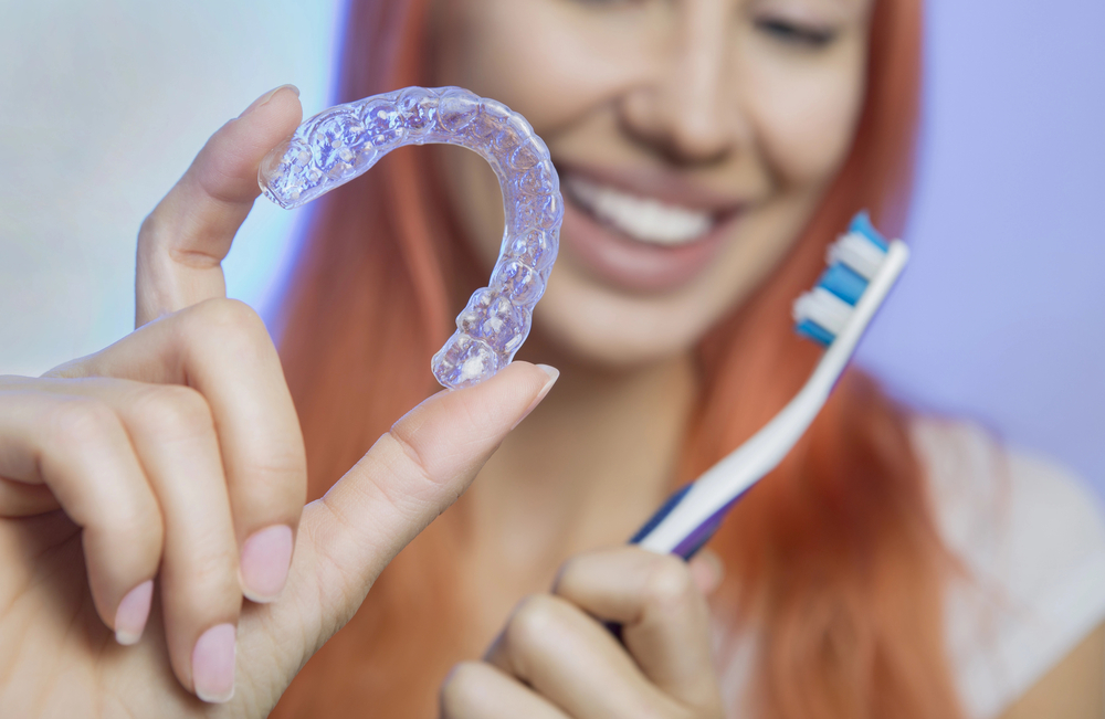 Teen smiles while holding up a toothbrush and Invisalign aligner.