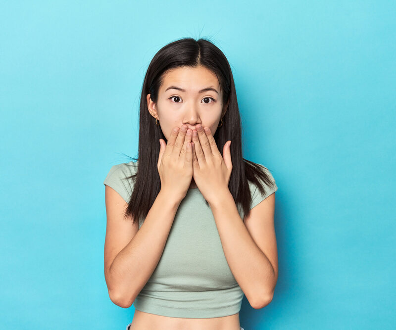 woman covering her mouth because of embarrassing smile on blue background
