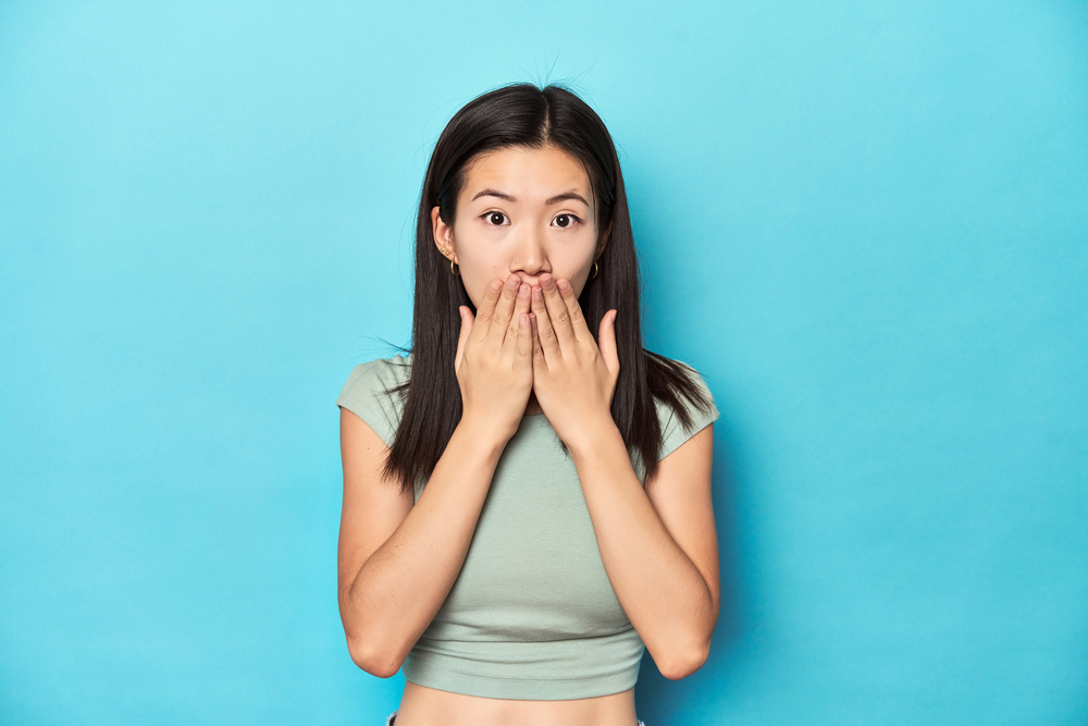 woman covering her mouth because of embarrassing smile on blue background