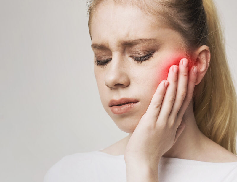 woman with jaw pain, holding her face, red spot on jaw