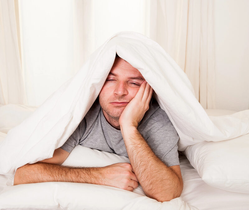 man laying in bed, holding head up with hand, blanket over his head, sleeping, sleep apnea