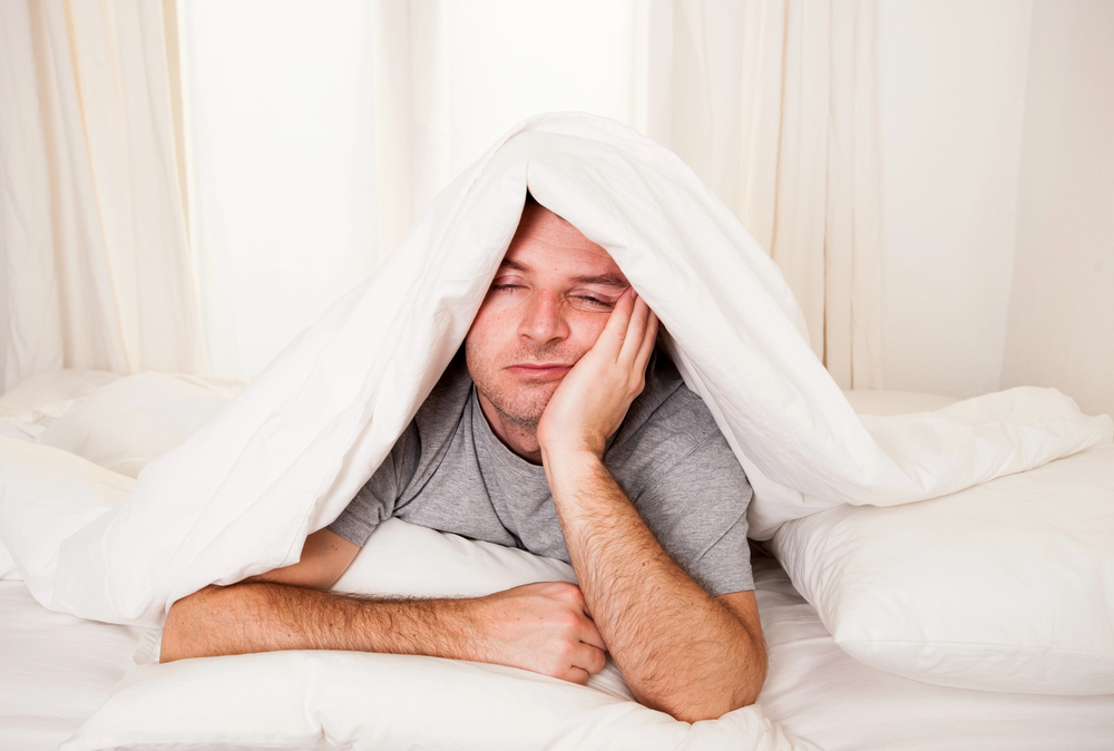 man laying in bed, holding head up with hand, blanket over his head, sleeping, sleep apnea