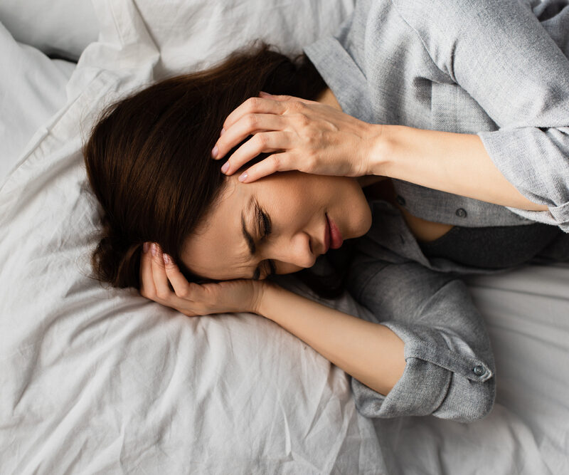 woman laying in bed, holding her head in pain