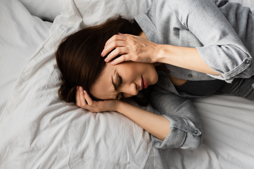 woman laying in bed, holding her head in pain