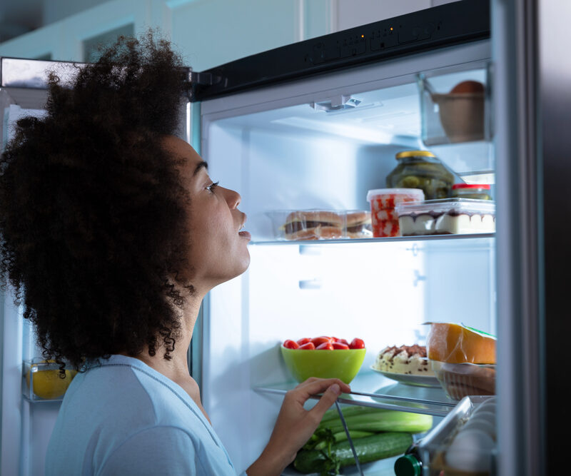 black woman with sleep apnea looking in fridge for a late night snack