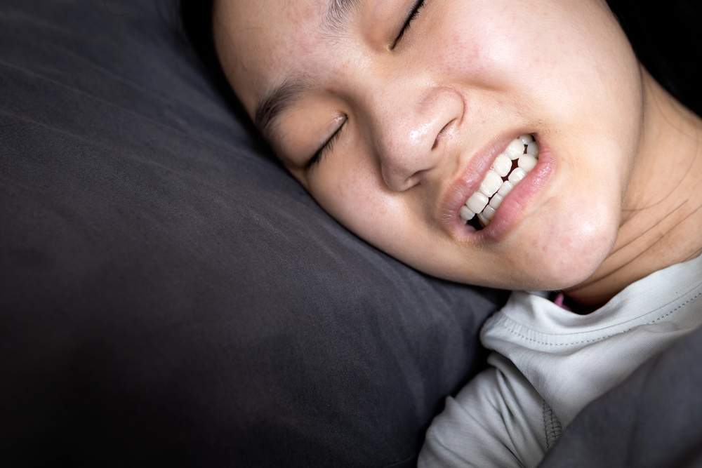 asian woman sleeping and grinding her teeth, wincing from jaw pain