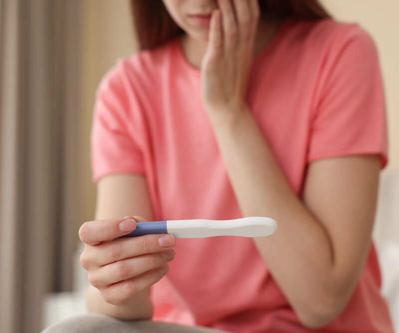 woman in pink shirt sitting on bed looking at pregnancy test result